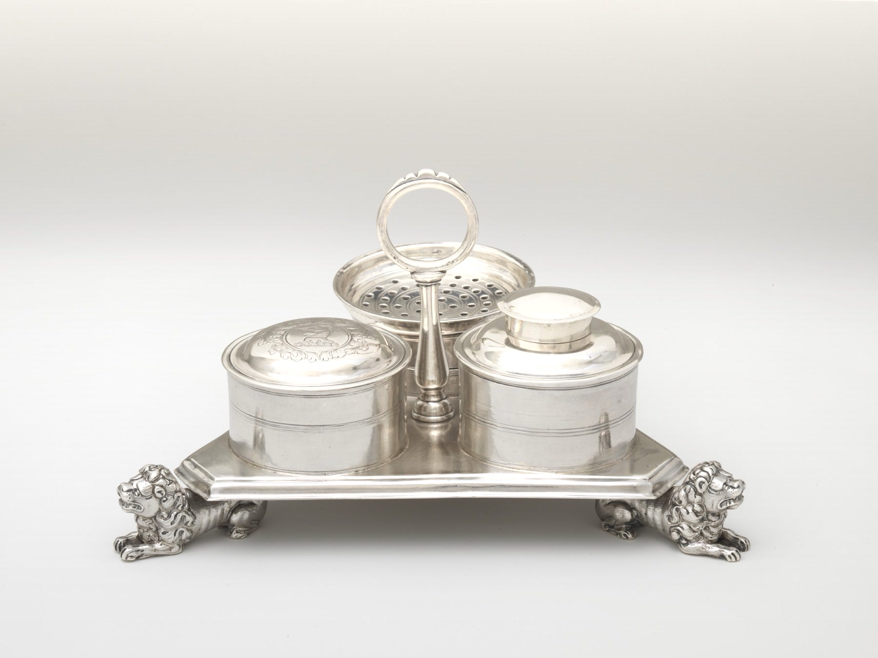 Tintero de plata de 1710 con dos tinteros, un salvadero y patas de león, fotografiado sobre fondo liso